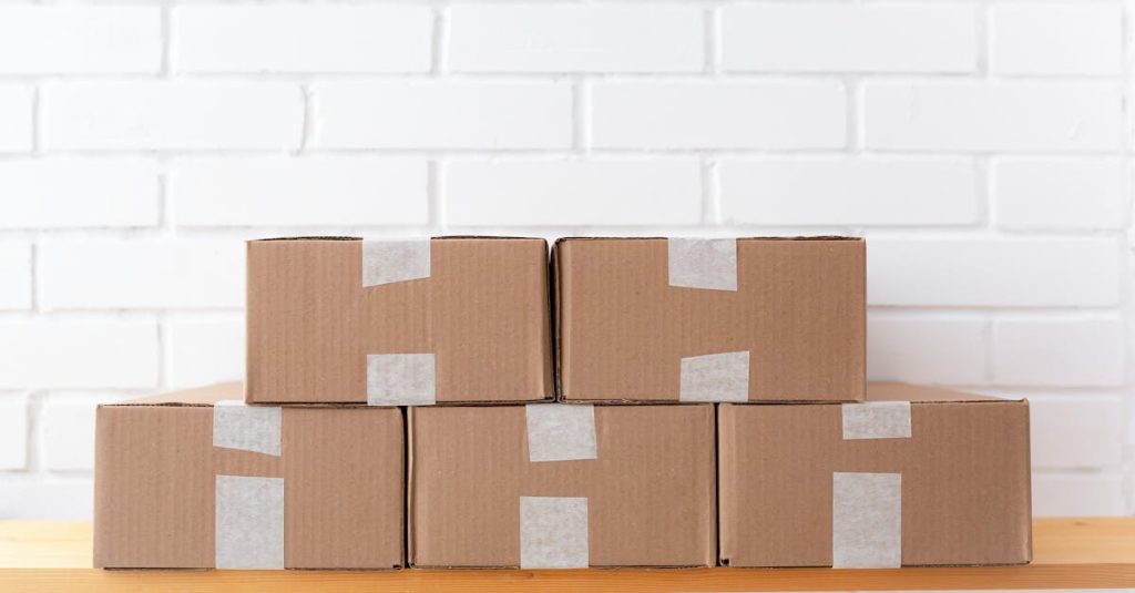 A neat stack of cardboard boxes taped and placed on a wooden shelf against a white brick wall.